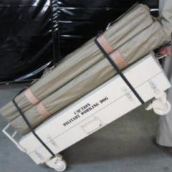 A wheeled storage container labeled "Caution Military Working Dog," possibly serving as a mobile kennel. The container holds cylindrical canvas items strapped securely to it, likely parts of the kennel setup. The unit is set within an indoor environment, possibly a warehouse or storage facility.