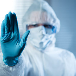 Person in white hazmat suit and blue gloves holding up left hand in stop gesture on blue gradient with white grid pattern background