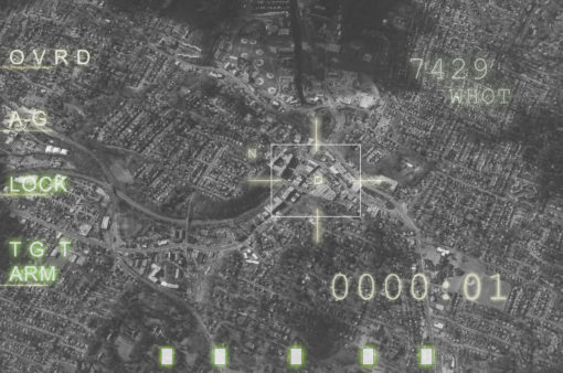 A black and white aerial view of a city with a military targeting overlay. The overlay includes a crosshair, text, and green lights at the bottom. The text on the overlay reads "OVRD", "AAG", "LOCK", "TGT", "ARM", "7429", "WHOT", and "0000-01". The green lights at the bottom appear to be indicators of some kind.