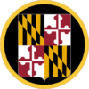 The image displays the logo of the Maryland National Guard, which features a shield bearing the Maryland state flag at its center. The shield is divided into four quadrants, with black and gold diagonal stripes in the top left and bottom right, and red and white crosses in the top right and bottom left. This shield is encircled by a gold outline, symbolizing unity and protection.